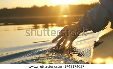 man puts fingers down in lake kayaking against backdrop of golden sunset, unity harmony nature