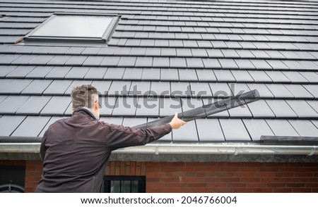 Man puts a gutter mesh to the rain gutter to protect the gutter from leaves. 