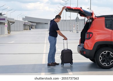 A Man Puts His Suitcase In The Trunk Of A Car In An Airport Parking Lot. Travel, Vacation Concept