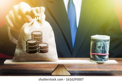 A Man Puts A Money Bag On The Scales Opposite To The Dollar. Exchange Rate, Comparison Of Economic Indicators. Avoiding Savings Inflation. Investments In Foreign Currency Bonds.