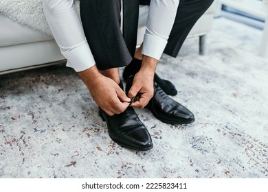 A man puts on black shoes in a hotel room. A man in a white shirt is tying shoelaces on leather shoes close-up. Businessman about to get dressed and going to a business meeting - Powered by Shutterstock