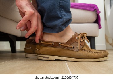 A Man Puts On Shoes With The Help Of His Toes: Boat Shoes On A Wooden Floor, While Inserting His Finger From The Back Between The Shoe And His Foot