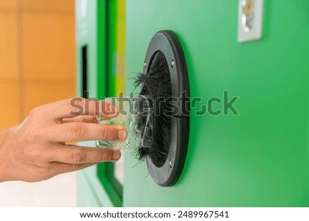 Man puts plastic bottle in a reverse vending machine. Male hand inserting reusable bottle into recycling machine to reduce waste. Close up. Sustainable lifestyle concept