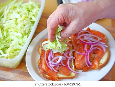 A Man Puts Shredded Lettuce On A Smoked Salmon Sandwich