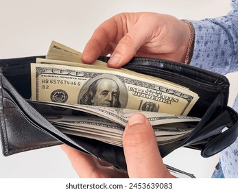 man puts stack of 100 dollars in his wallet.  Rational spending of money, business man