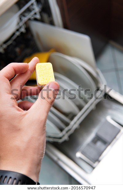 the man puts a tablet in the dishwasher.\
washing dishes in a\
dishwasher\
