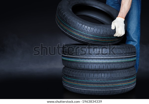 Man puts a tire in a stack of tires on\
creative black background. Tire changing\
concept