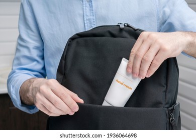 Man puts tube hand cream in a backpack, male hands, cropped image, close-up