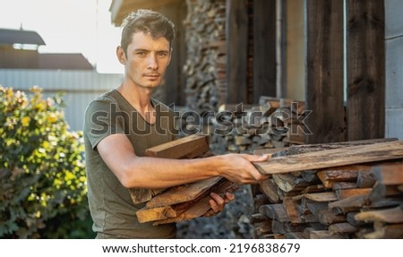 A man puts wood in hands from a woodpile for a home fireplace. The concept of wood-burning heating and the energy crisis