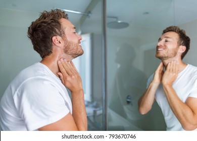 Man Putting After Shave Perfume Lotion Or Skin Care Cream For Sensitive Skin After Shaving Beard Looking In Bathroom Mirror On Neck. Male Beauty, Beard Care Skincare Concept.