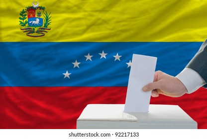 Man Putting Ballot In A Box During Elections In Venezuela In Front Of Flag