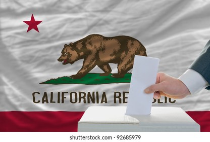 man putting ballot in a box during elections  in front of flag american state of california