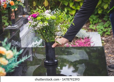 Man Is Putting Bouquet Of Flowers On Headstone At Cemetery. Sadness For Dead Person At All Souls Day. Flower Arrangement At Tombstone