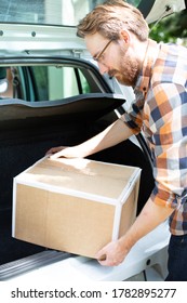 Man Putting Cardboard Package, Box Into The Trunk, Boot Of A Car.