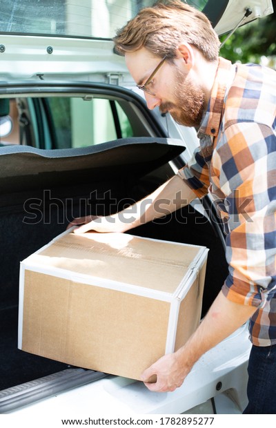 Man putting cardboard package, box into the trunk,\
boot of a car.