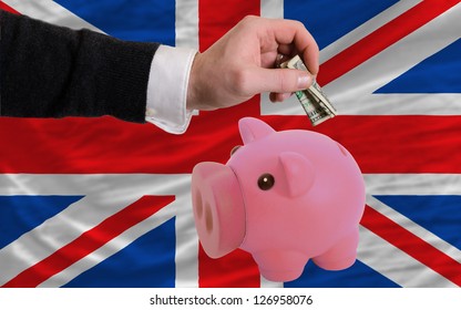 Man Putting Dollar Into Piggy Rich Bank National Flag Of Uk In Foreign Currency Because Of Inflation