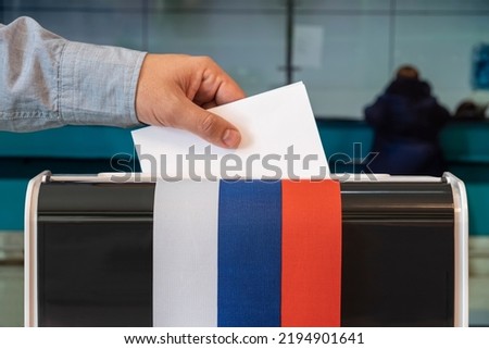 man putting electoral billuten in a box during elections in russia. russia flag. voters to vote on a single voting day in Russia at a polling station