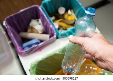 Man Putting Empty Plastic Bottle In Recycling Bin In The Kitchen. Person In The House Kitchen Separating Waste. Different Trash Can With Colorful Garbage Bags. Top View