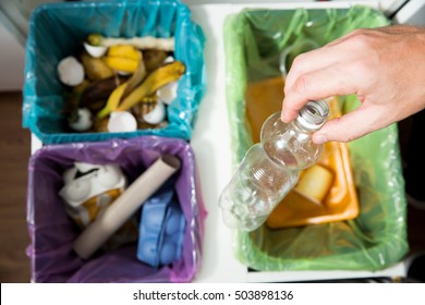 Man Putting Empty Plastic Bottle In Recycling Bin In The Kitchen. Person In The House Kitchen Separating Waste. Different Trash Can With Colorful Garbage Bags. Top View