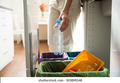 Man putting empty plastic bottle in recycling bin in the kitchen. Person in the house kitchen separating waste. Different trash can with colorful garbage bags. 