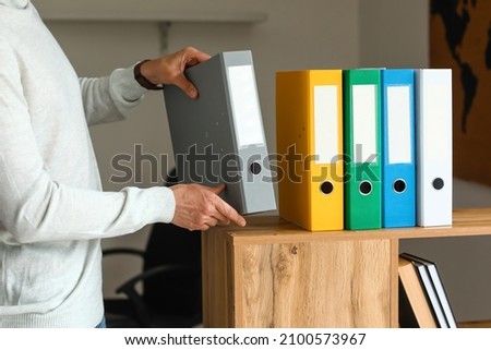 Man putting folder with documents on shelf in office