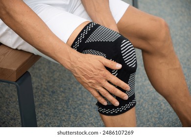 Man putting knee brace to support painful leg. Athlete bodybuilder leg wearing knee support brace or elastic kneecap bandage. Sleeve for compression. Health problems and pain. - Powered by Shutterstock