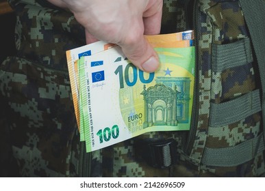 Man Is Putting In A Military Backpack Euros. Dark Green Camouflage Khaki Bag With Money. Migrants And Refugees Concept. Looting And Robbery.