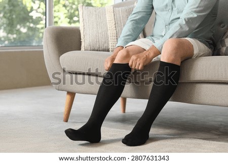Man putting on black compression socks while sitting on sofa
