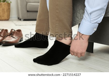 Man putting on black socks at home, closeup