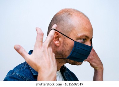 Man Putting On A Cloth Face Mask For Virus Protection, White Background.