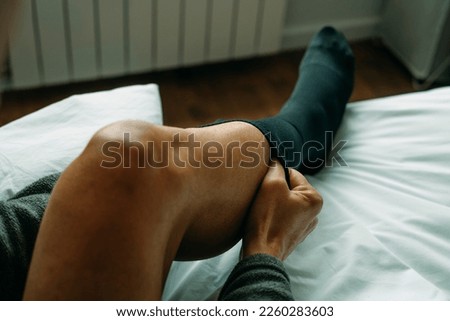 a man is putting on a compression sock sitting on his bed at home