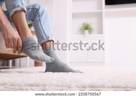 Man putting on grey socks at home, closeup. Space for text