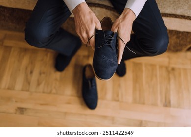 A man is putting on his shoes. The shoes are black and have a lace. The man is sitting on a couch - Powered by Shutterstock