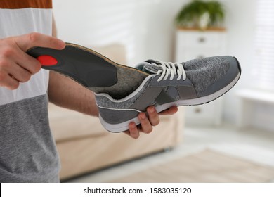 Man putting orthopedic insole into shoe at home, closeup