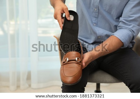 Man putting orthopedic insole into shoe indoors, closeup. Foot care