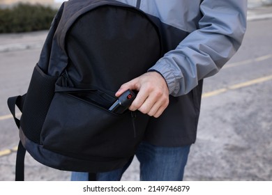 Man putting pepper spray into backpack outdoors, closeup