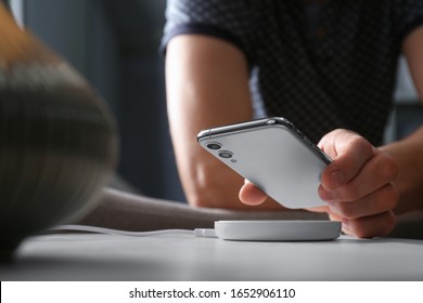 Man putting smartphone on wireless charger in room, closeup