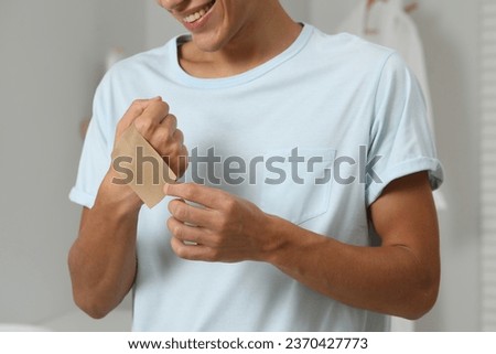 Man putting sticking plaster onto hand indoors, closeup