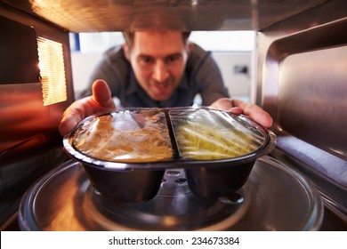 Man Putting TV Dinner Into Microwave Oven To Cook