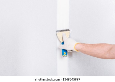 Man with putty knife shows how to hide the connection place between two pieces of dry walls using putty and construction tape