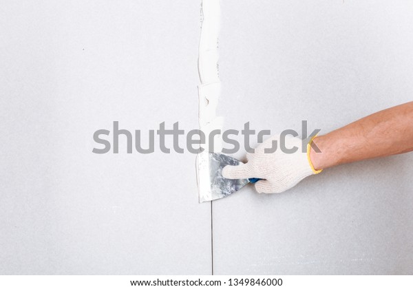 Man\
with putty knife shows how to hide the connection place between two\
pieces of dry walls using putty and construction\
tape