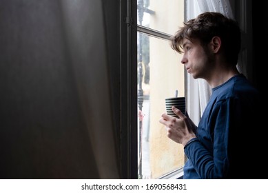 Man In Pyjamas Looking Through The Window During Quarentine