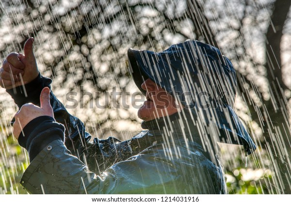 Man in rainwear raincoat and rain hat doing\
thumbs up signaling to\
someone