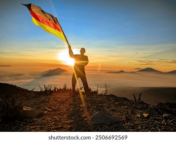 man raising the flag of Germany, on the top of the mountain. background of mountains at sunset or sunrise. Germany flag for Independence Day. - Powered by Shutterstock