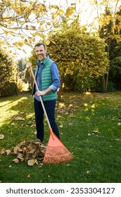 Man raking leaves in garden smiling at camera during fall autumn backyard cleanup