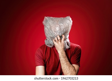 The man reaches for his mouth, feeling suffocated in a plastic bag. Red background. Copy space. Concept of pollution and environmental protection.