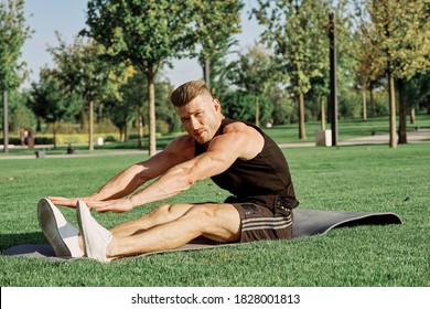 A man reaches for the tips of his toes in nature in the park on the grass