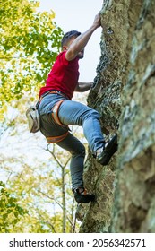 Man reaching for a grip while he rock climbs on a steep cliff