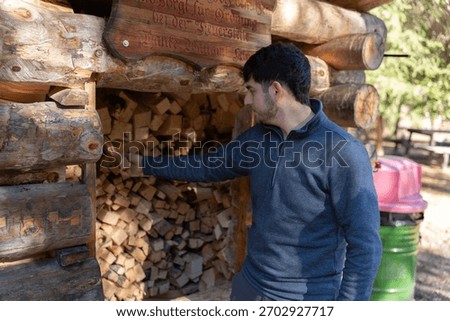 Man reaching for logs stacked in a rustic woodshed, preparing for fire