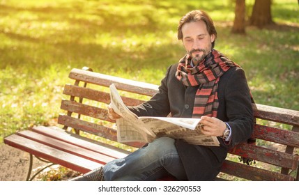 Man Reading About The Current Events In The Newpaper In The Park. Handsome Man Resting On The Bench In Autumn Season.